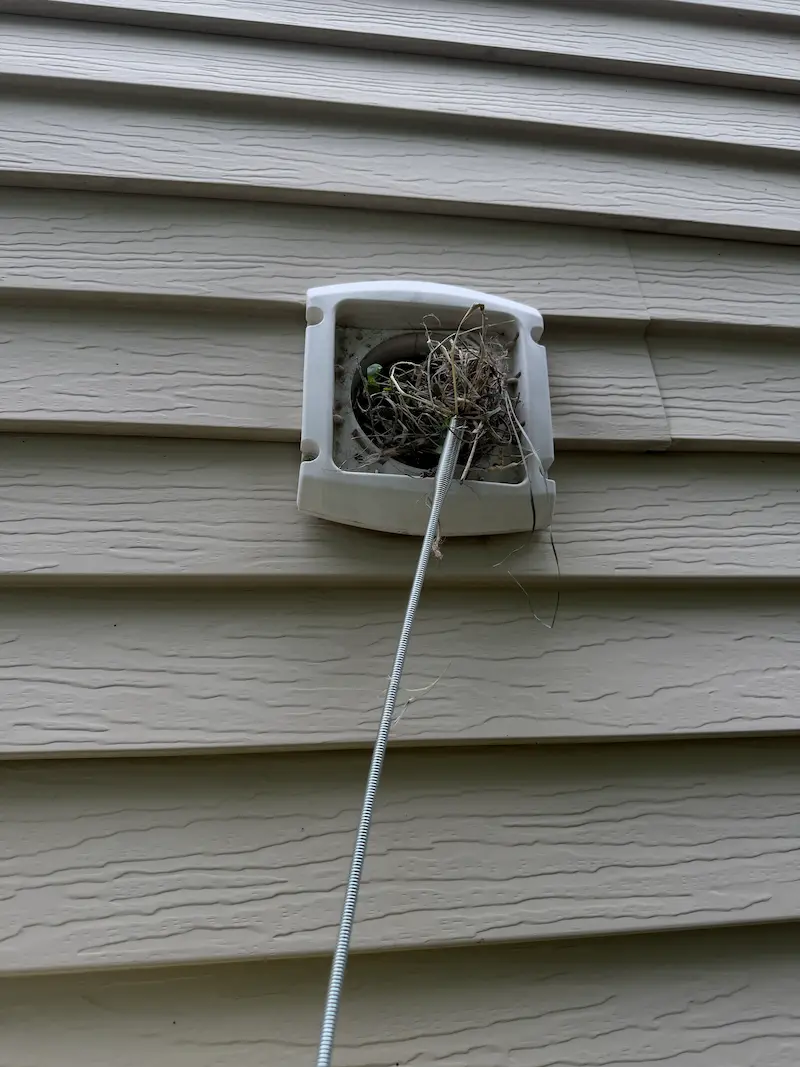 Bird nest packed inside an exterior dryer vent hood, with a cleaning rod inserted to clear the run