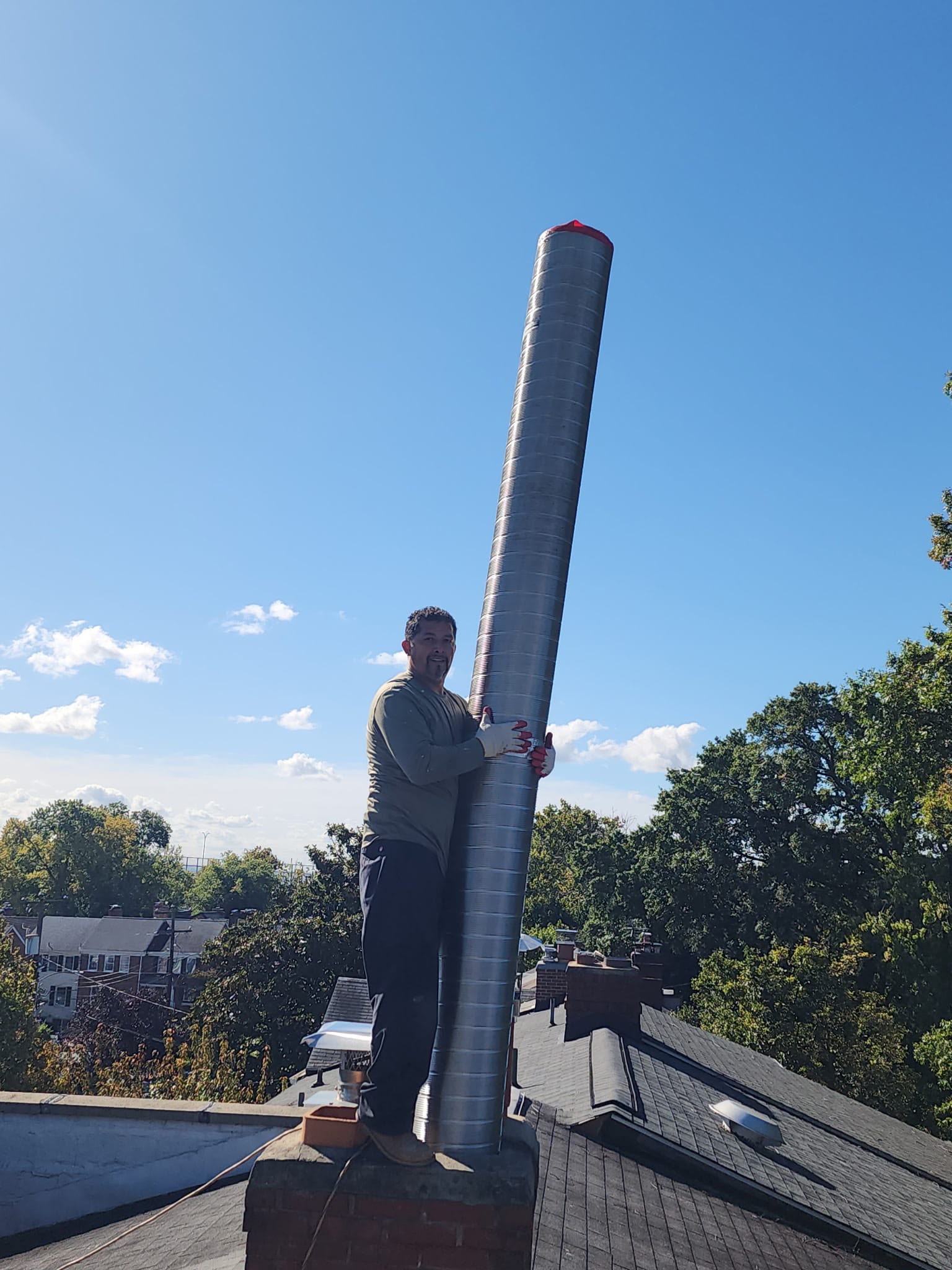 CleanFlow Pros technician installing a new stainless steel chimney liner down the flue on an Alexandria rooftop