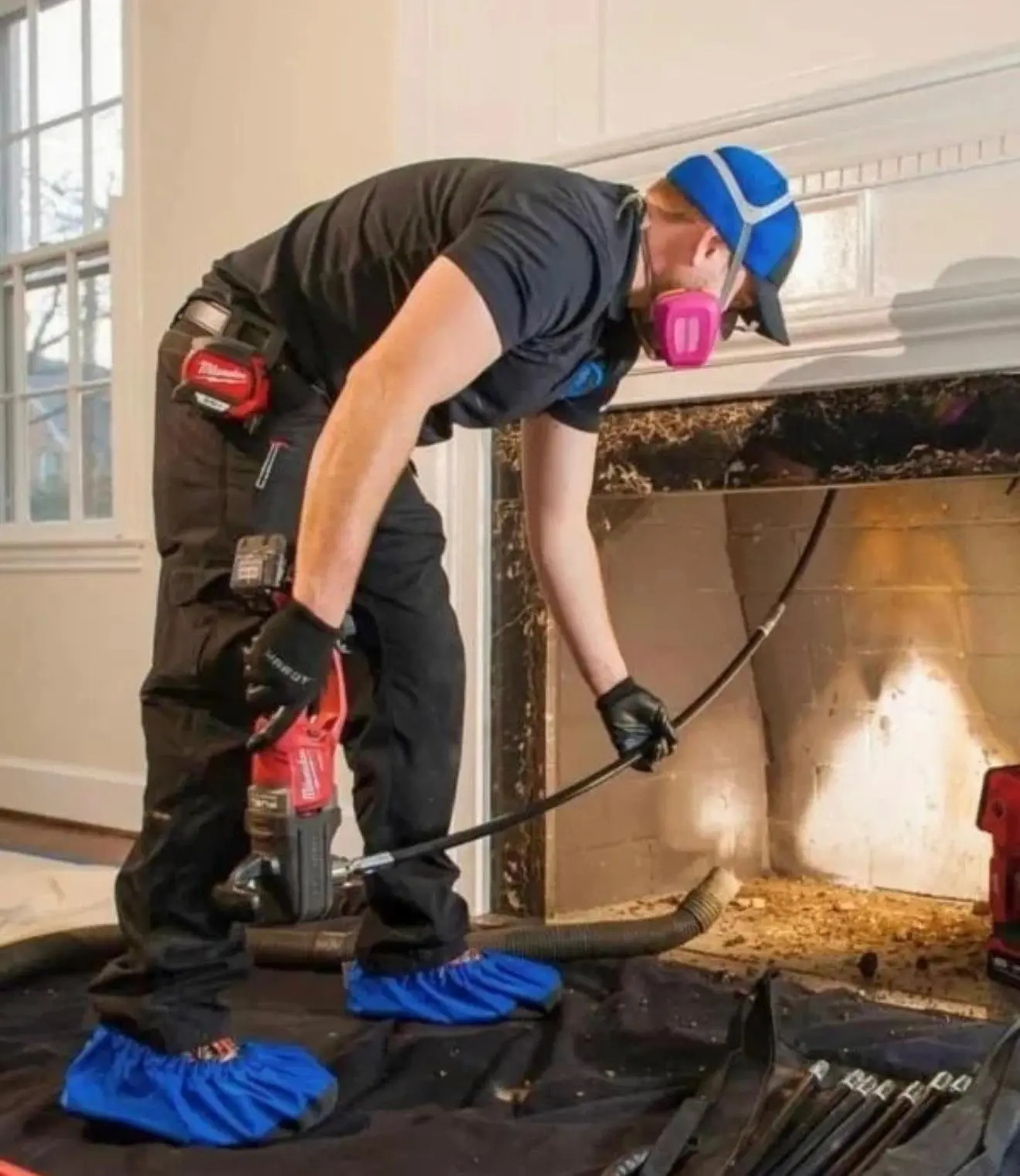 CleanFlow Pros technician running a rotary sweep rod up a firebox flue with drop cloths protecting the floor