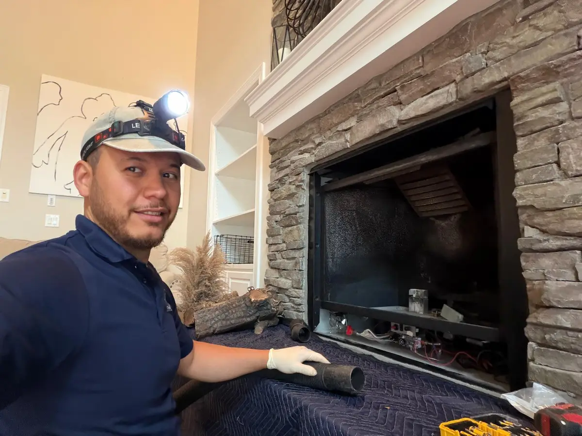 Technician servicing a gas fireplace with the glass front removed, showing the burner assembly