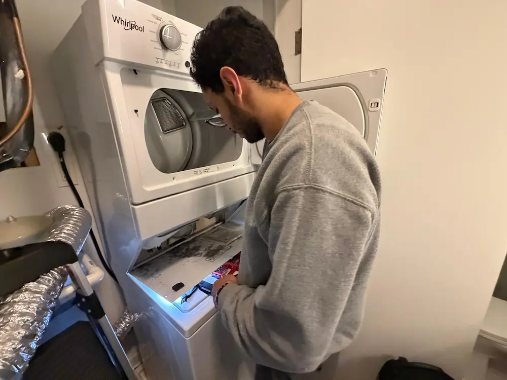 Technician checking a stacked dryer with the lower panel removed to diagnose slow drying